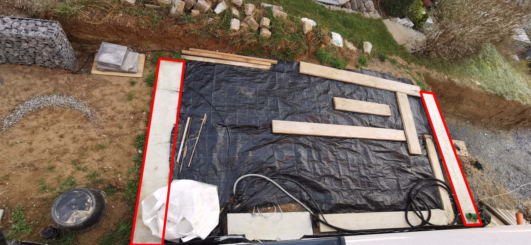 Baustelle mit Fundamenten, Holzbalken und schwarzer Baufolie auf einer Baugrube