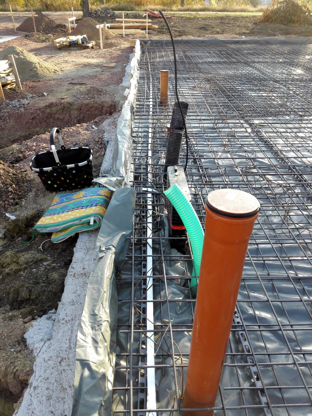 Baustelle mit Fundamentbewehrung aus Stahl, Rohrleitungen und Bauwerkzeugen auf einer Baugrube.