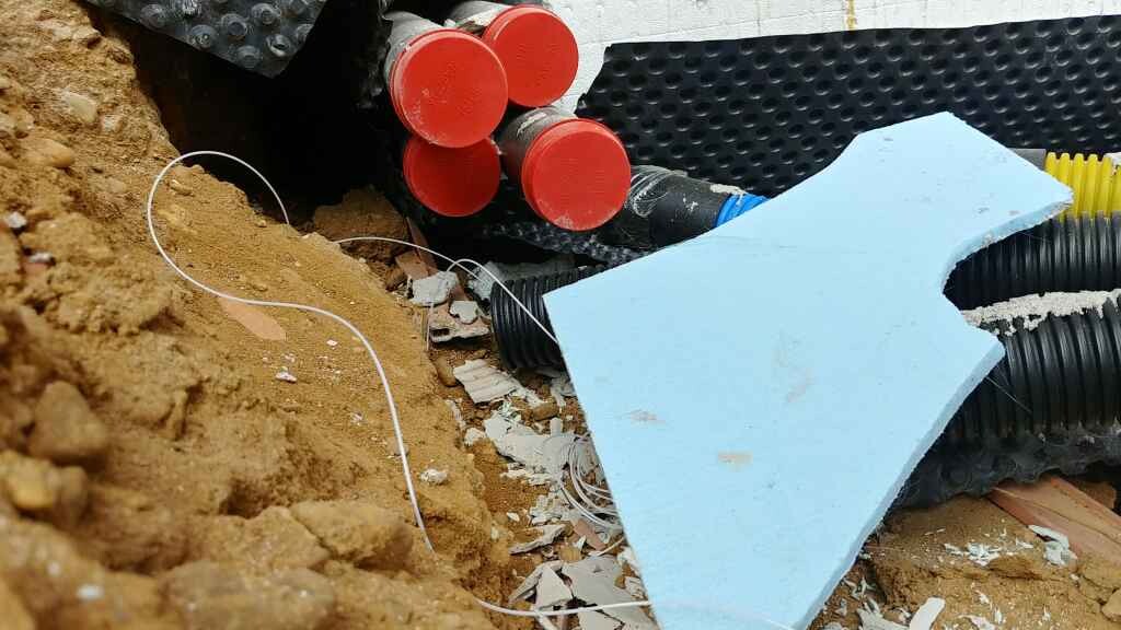 Baustelle mit Erde, Rohre, Dämmplatten und Kabel in Baugrube