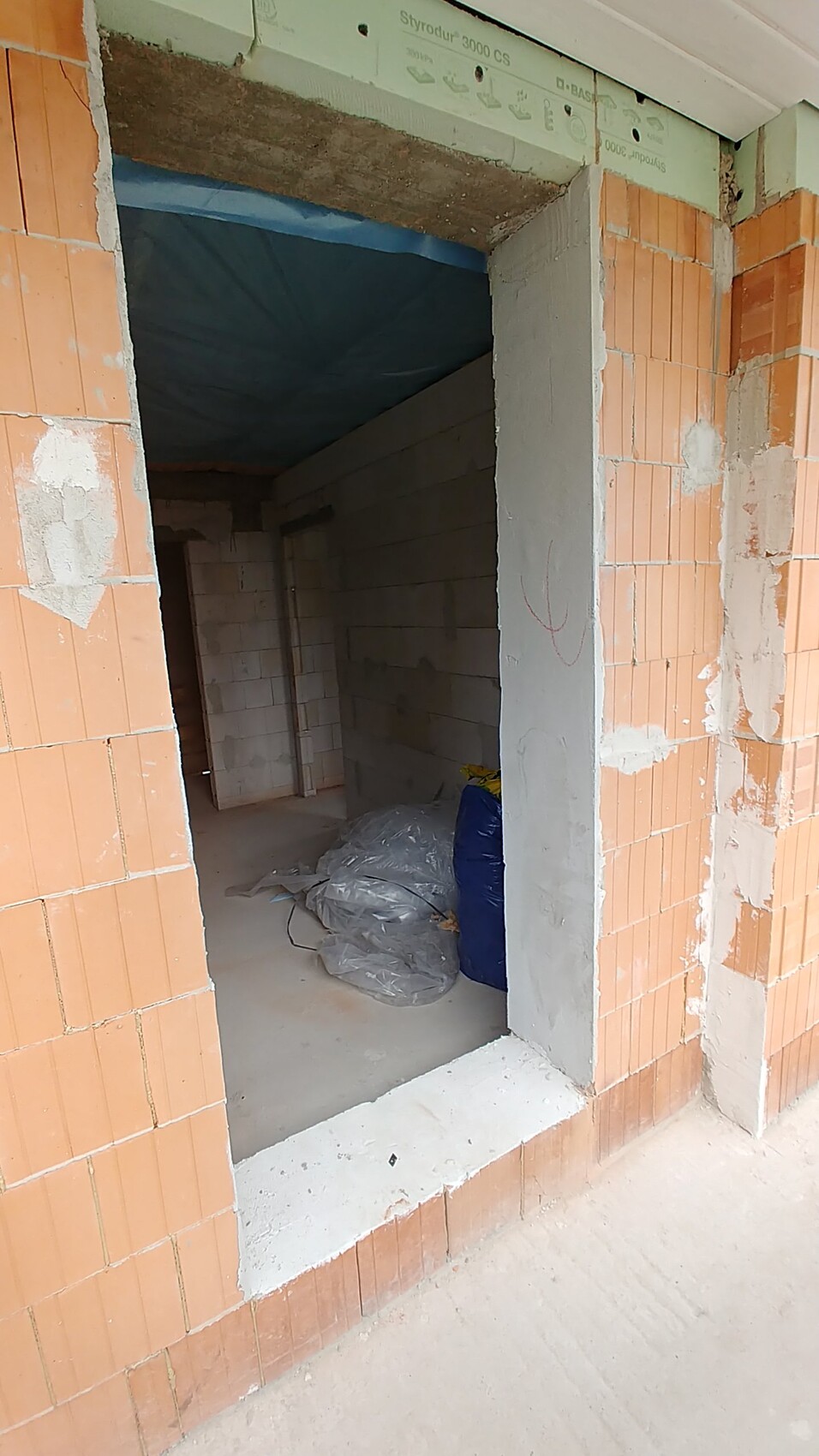 Baustelle im Rohbau: offener Türdurchgang, Ziegelwände und Baustoffe im Innenbereich