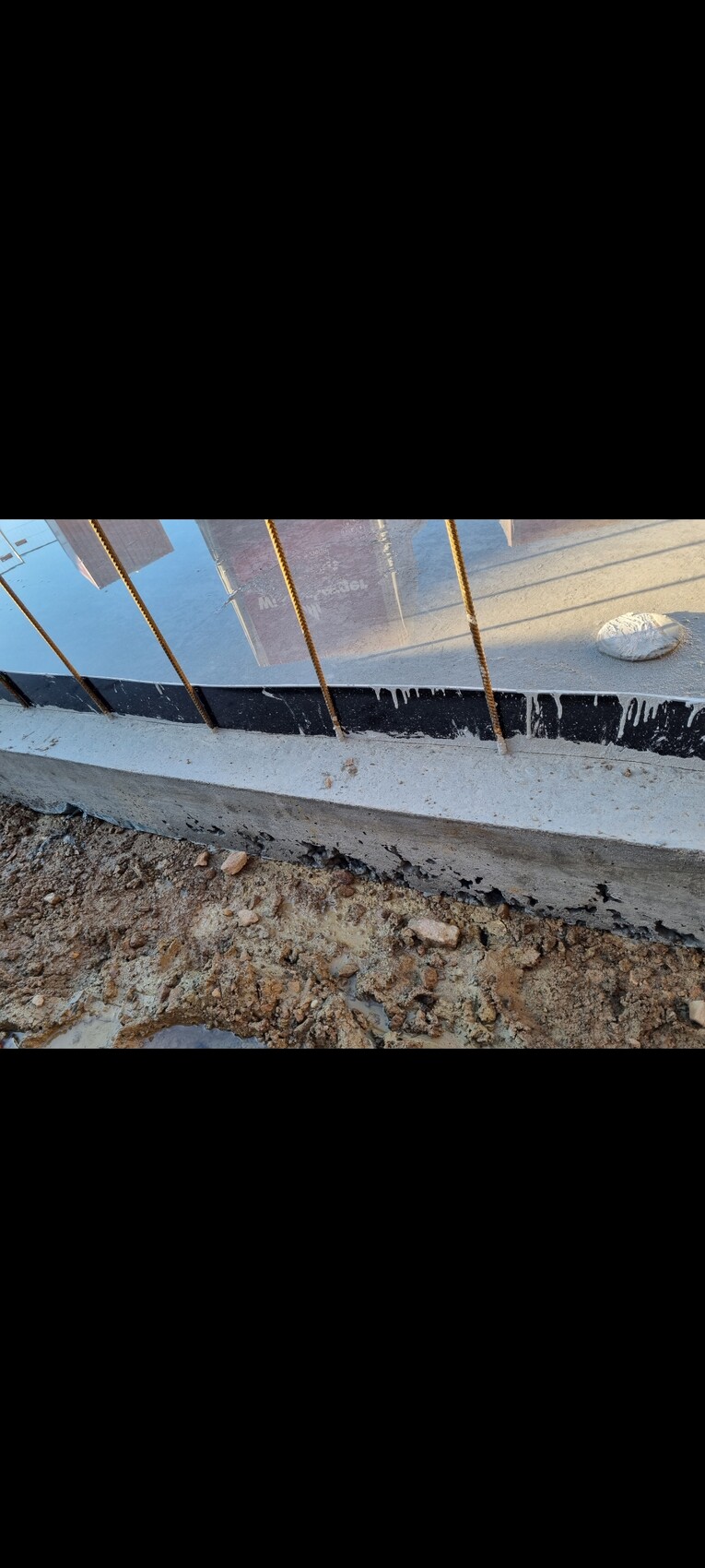 Bewehrungsstahl ragt aus einer Betonfundamentkante auf einer Baustelle; Erdreich daneben.