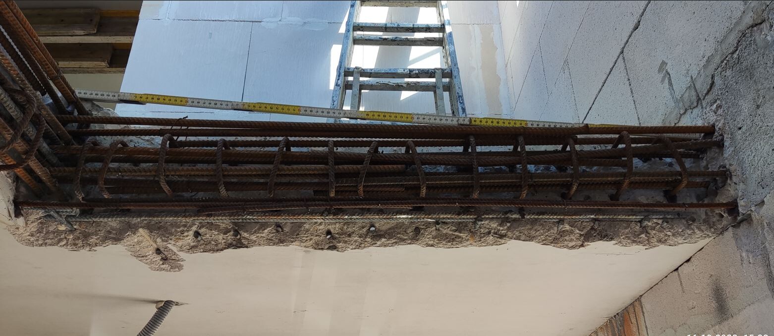 Rostige Bewehrungsstäbe ragen aus einer Betonplatte; im Hintergrund eine Leiter.