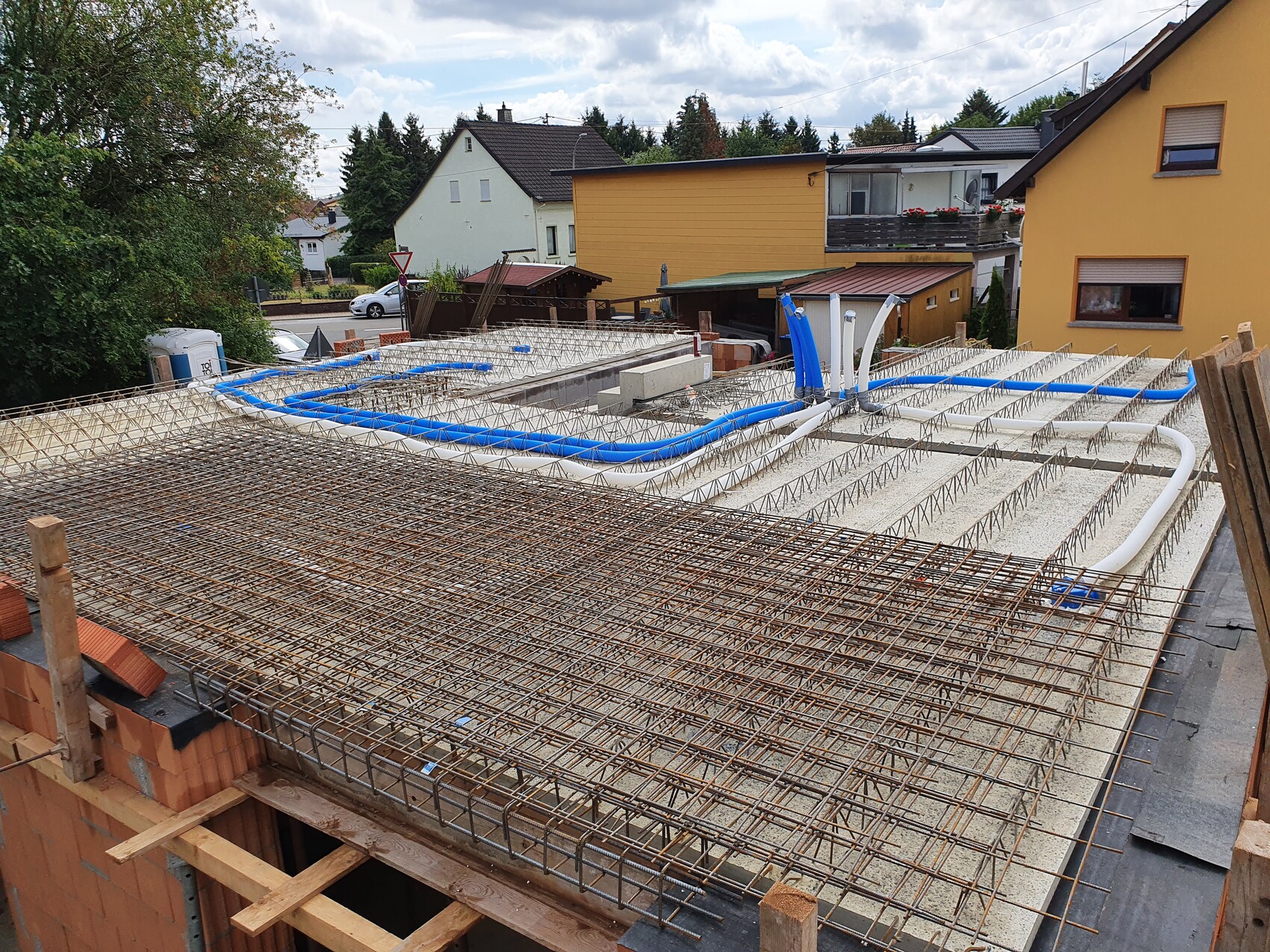 Stahlbewehrung und blaue Rohre auf Dachkonstruktion eines Bauprojekts, umliegende Häuser.