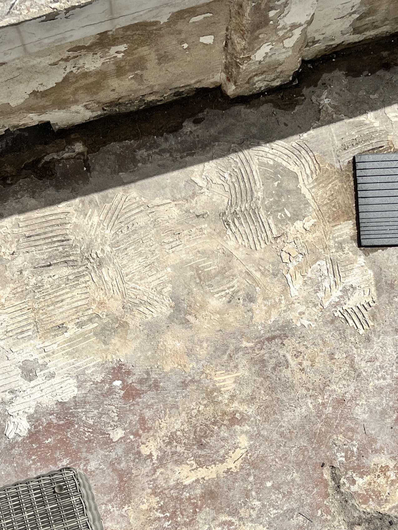 Betonboden mit kreisförmigen Rillenmustern, abgeblättert, Schatten; rechts dunkler Streifen.