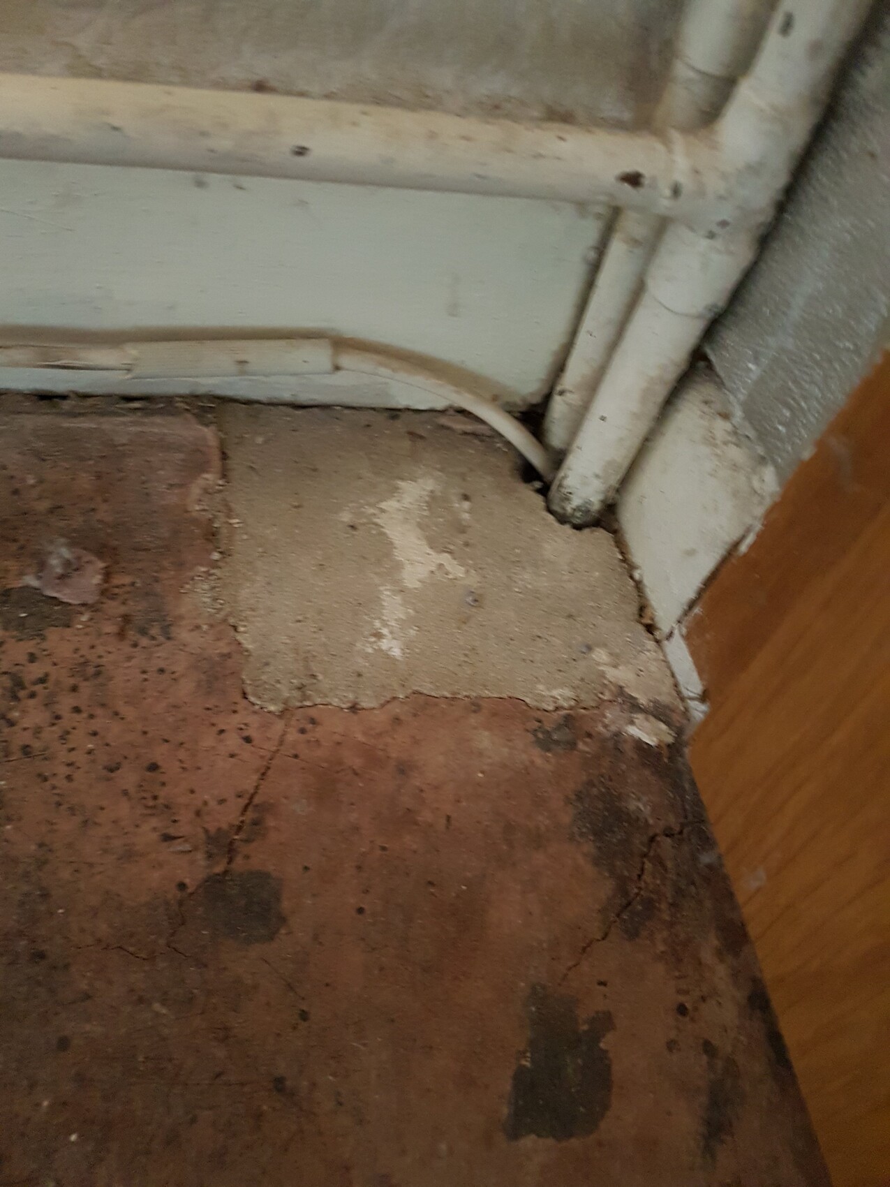 Unbearbeiteter Rohbau-Boden mit Rissen neben Wand und Türrahmen