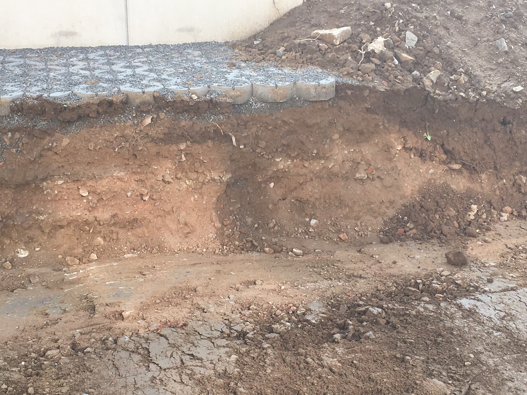 Ausgehobene Baugrube mit Erdschichten neben Betonwand, Kies und Pflastersteinen