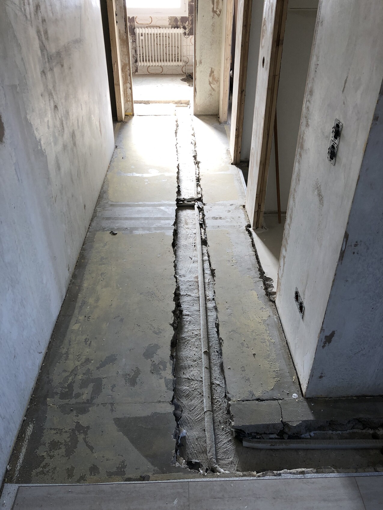 Flur einer Baustelle mit langem Bodenkanal und Rohr in der Betonfläche.