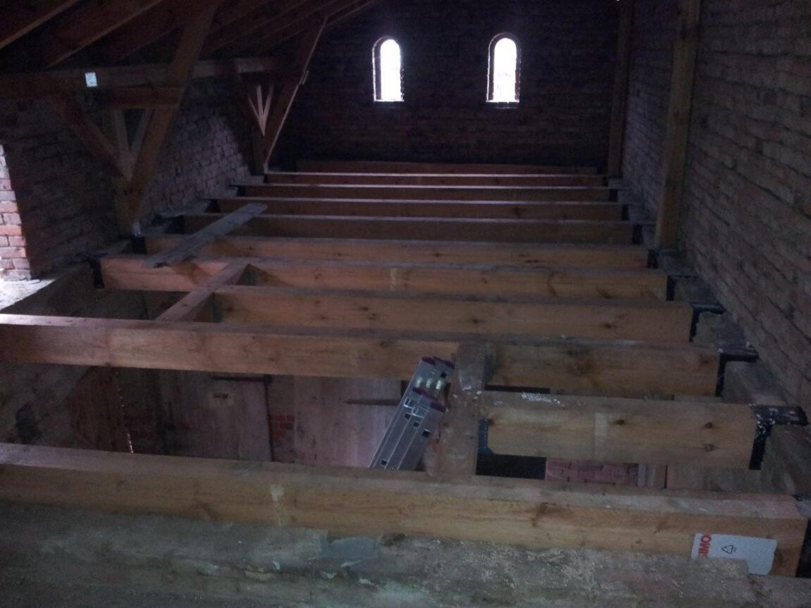 Dachboden mit offenen Holzbalken, Bruchsteinwänden und kleinen Dachfenstern am Ende