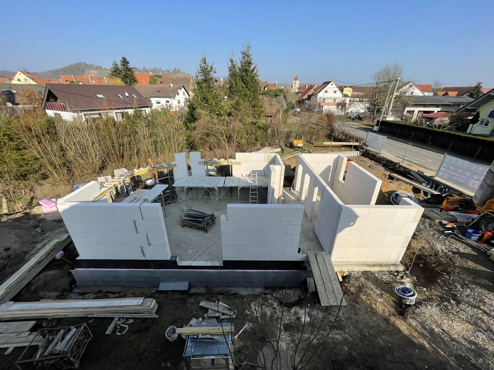 Rohbau eines Hauses aus weißen Porenbetonblöcken; Baugerüste und Baumaterialien auf der Baustelle.