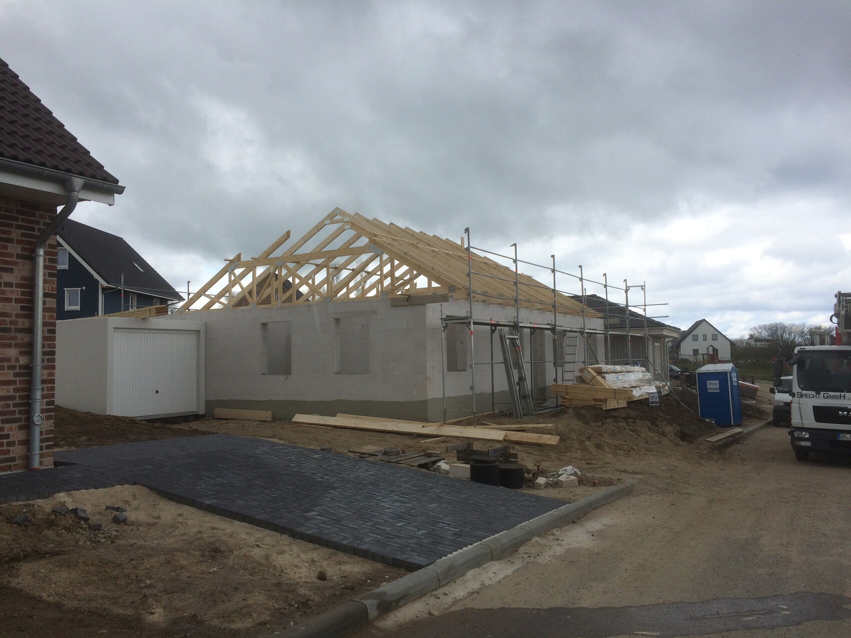 Wohnhaus-Rohbau mit Holz-Dachstuhl, Gerüst und Baumaterialien.