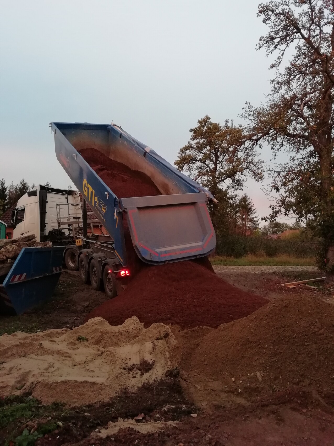 Blauer Kipplader-LKW kippt rotes Erdmaterial auf einen Haufen bei Bauarbeiten.