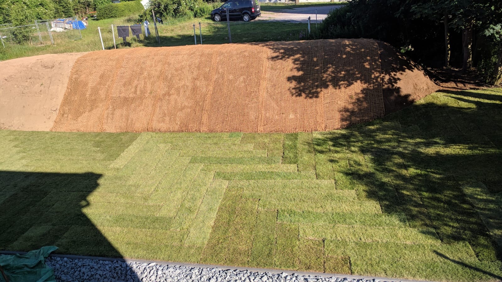 Großer Erdwall auf Baugrundstück mit Netzhülle und Gartenbereich im Vordergrund