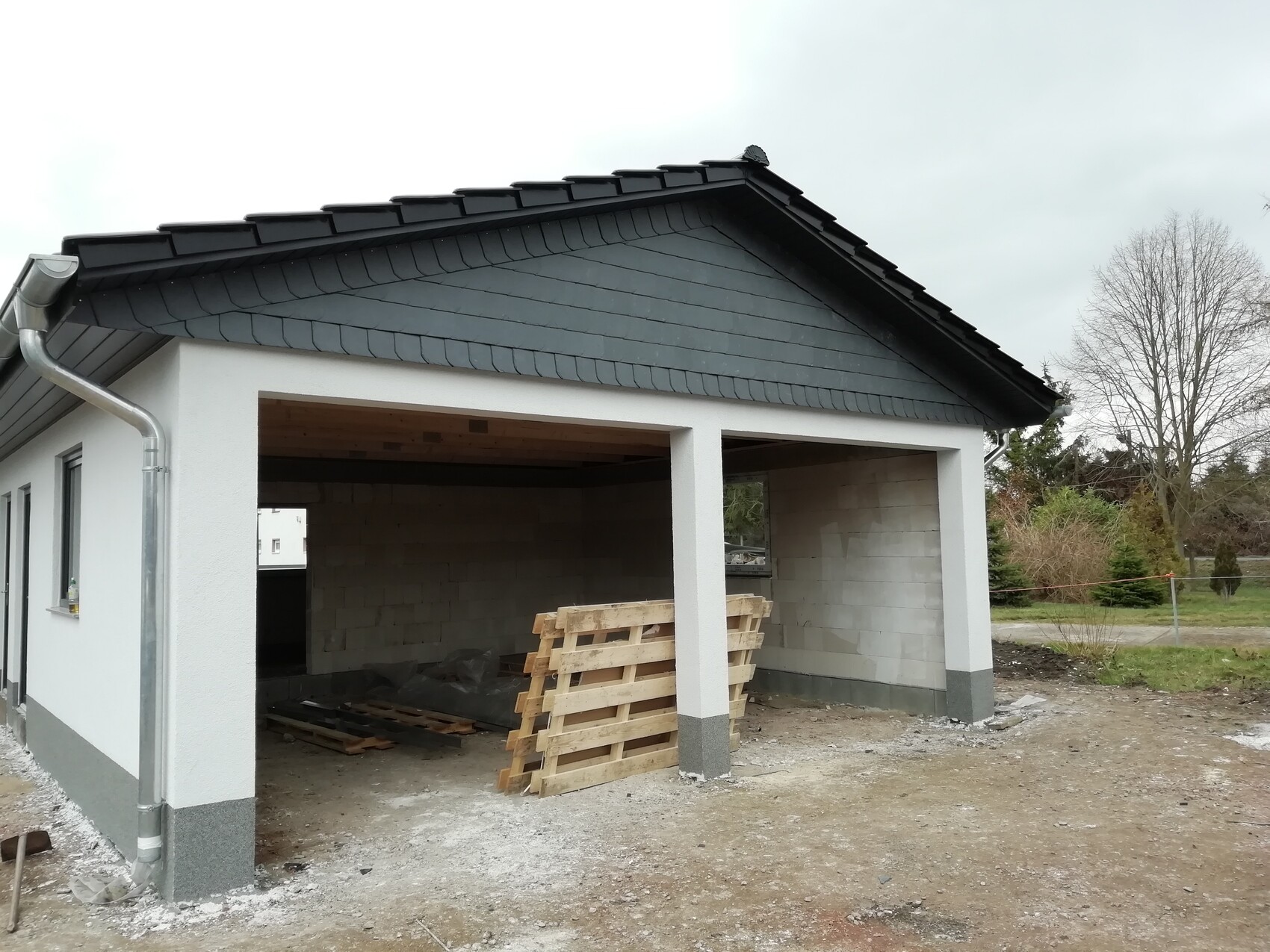 Neubau-Garage: weiße Außenwand, dunkles Dach, offener Innenraum mit Paletten