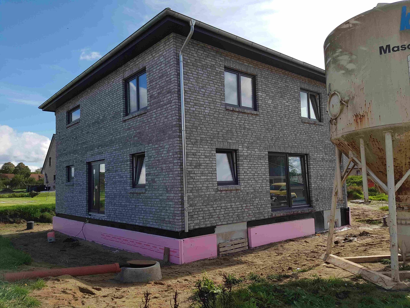 Zweistöckiges Haus im Rohbau mit Ziegeloptik und Baugrund sichtbar