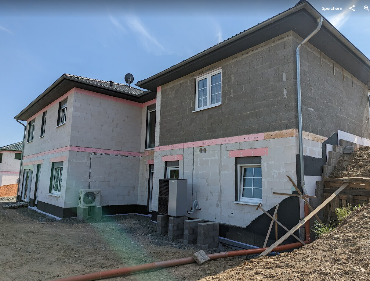 Zweistöckiges Haus im Rohbau mit sichtbaren Dämmplatten, Fenstern und Baugeräten.