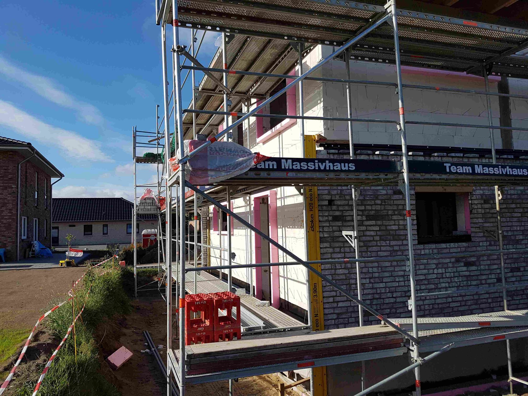 Baugerüst um ein Haus im Rohbau mit Baustoffen auf einer Baustelle