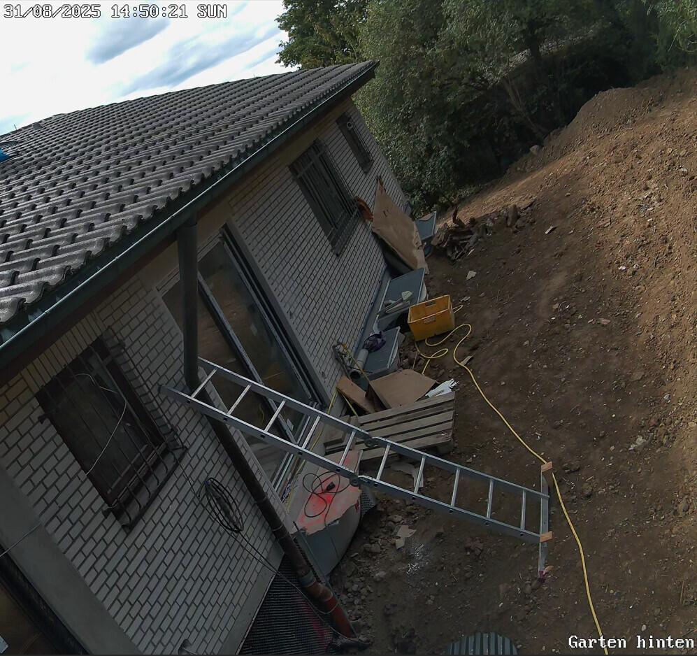 Außenansicht eines Einfamilienhauses im Bau mit Leiter und Baugeräten im Gartenbereich.