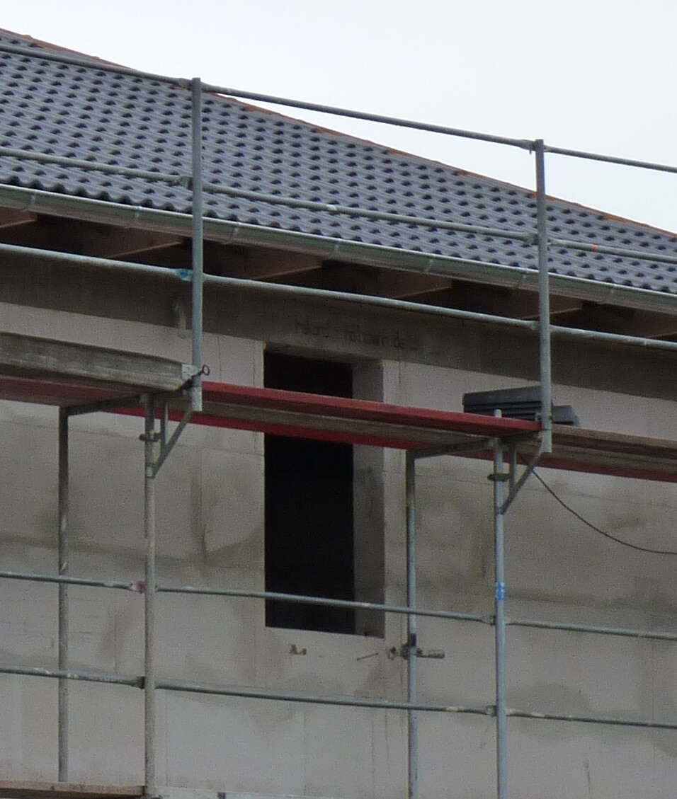 Baustelle mit Gerüst rund um unfertiges Haus, sichtbares Dach mit Ziegeln
