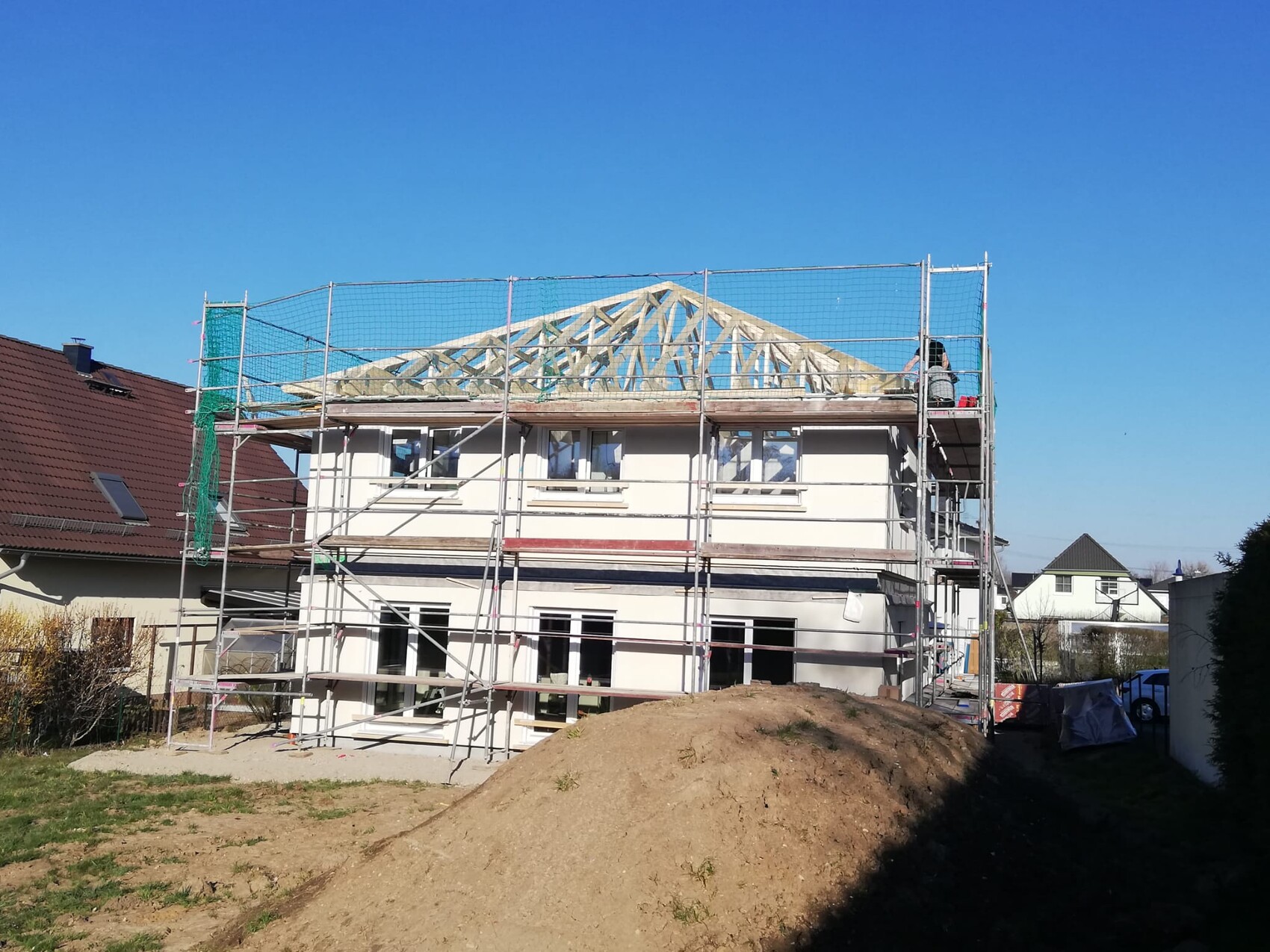 Zweistöckiges Haus mit Gerüst; Dachstuhl wird aufgebaut, blauer Himmel im Hintergrund