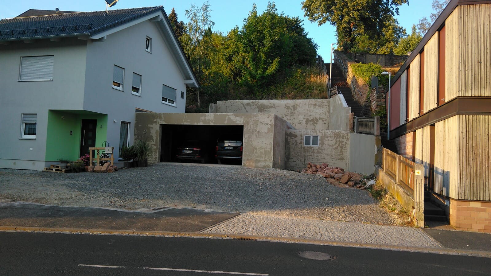 Wohnhaus neben Rohbau-Fundamentarbeiten, Garagenbereich und Kiesfläche