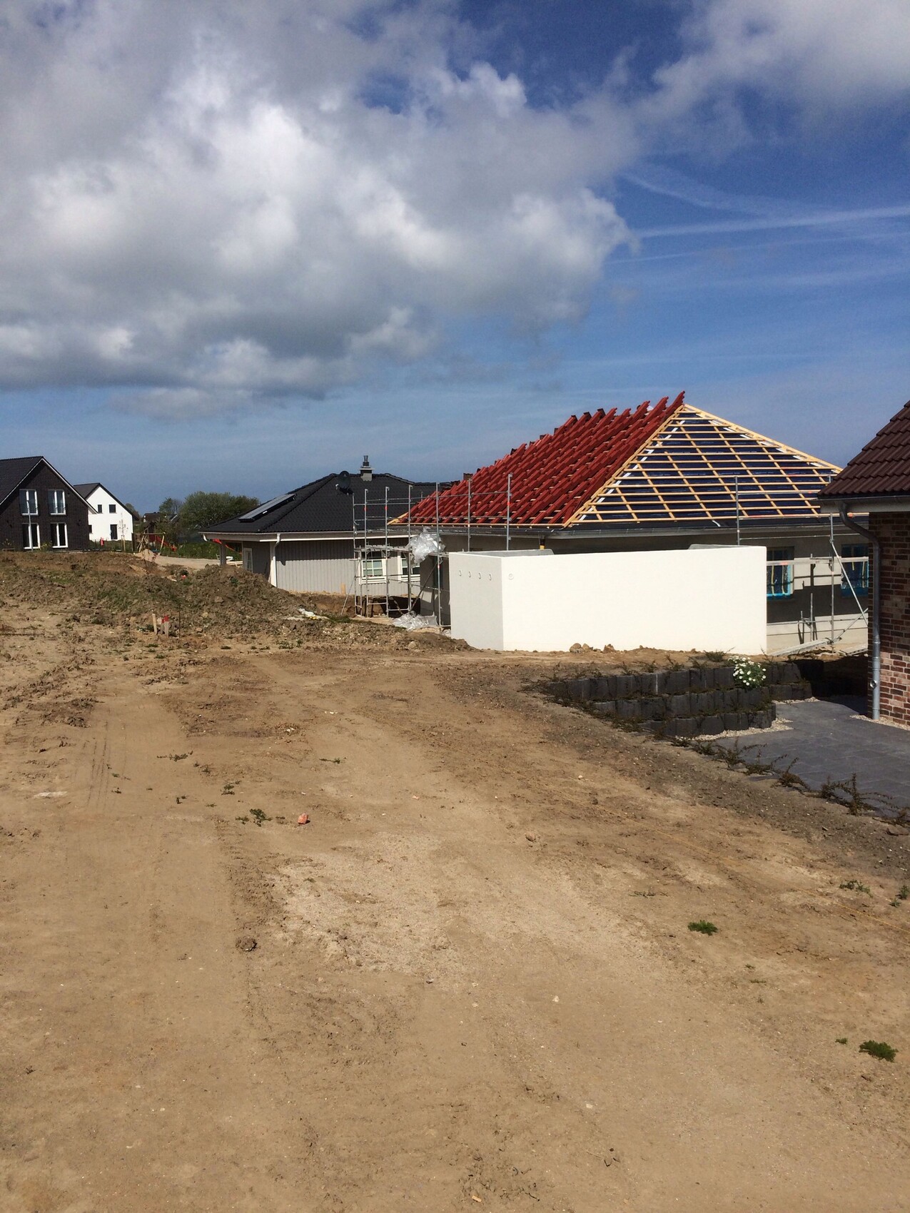 Baustelle mit rotem Dachstuhlgerüst, Gerüsten und freier Erdfläche vor Neubauhäusern.