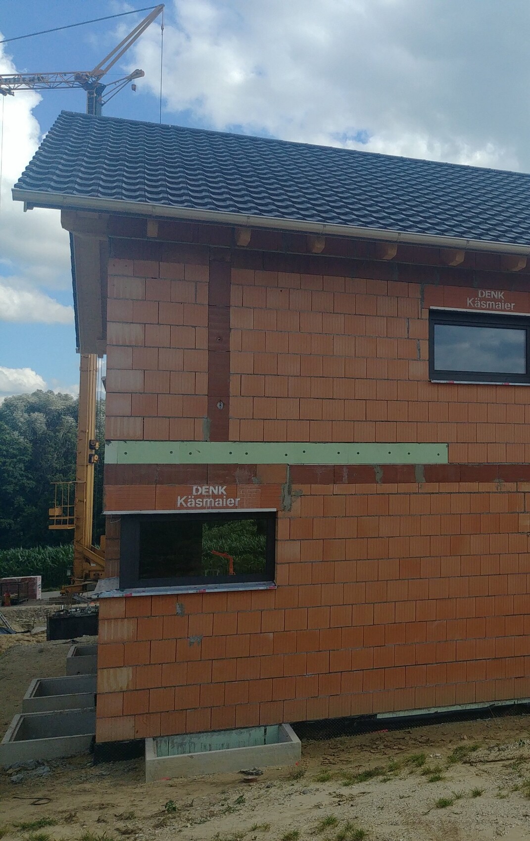 Unterbau eines Rohbaus mit Ziegelwänden, Dachziegeln und Baukran im Hintergrund.