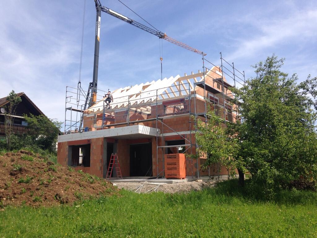 Rohbau eines Mehrfamilienhauses mit Gerüst, Kran und Bauarbeitern beim Dachaufbau