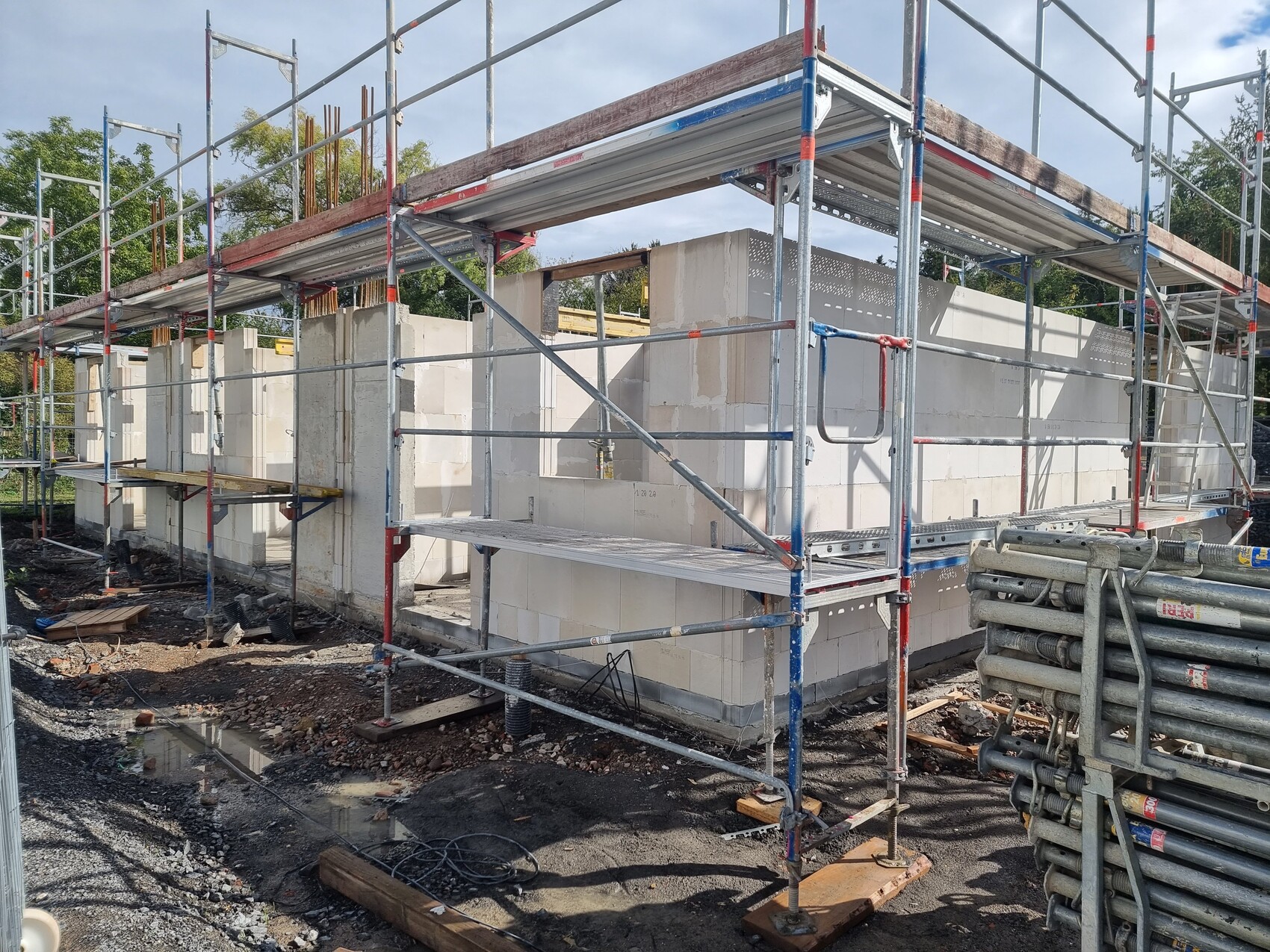 Baugerüst um ein halbfertiges Gebäude aus Betonblöcken auf einer Baustelle; Boden mit Wasserpfütze.