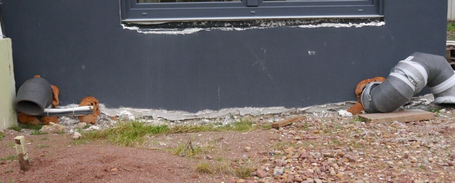 Außenwand mit Rohbaufundament und sichtbaren Rohrleitungen am Gebäude
