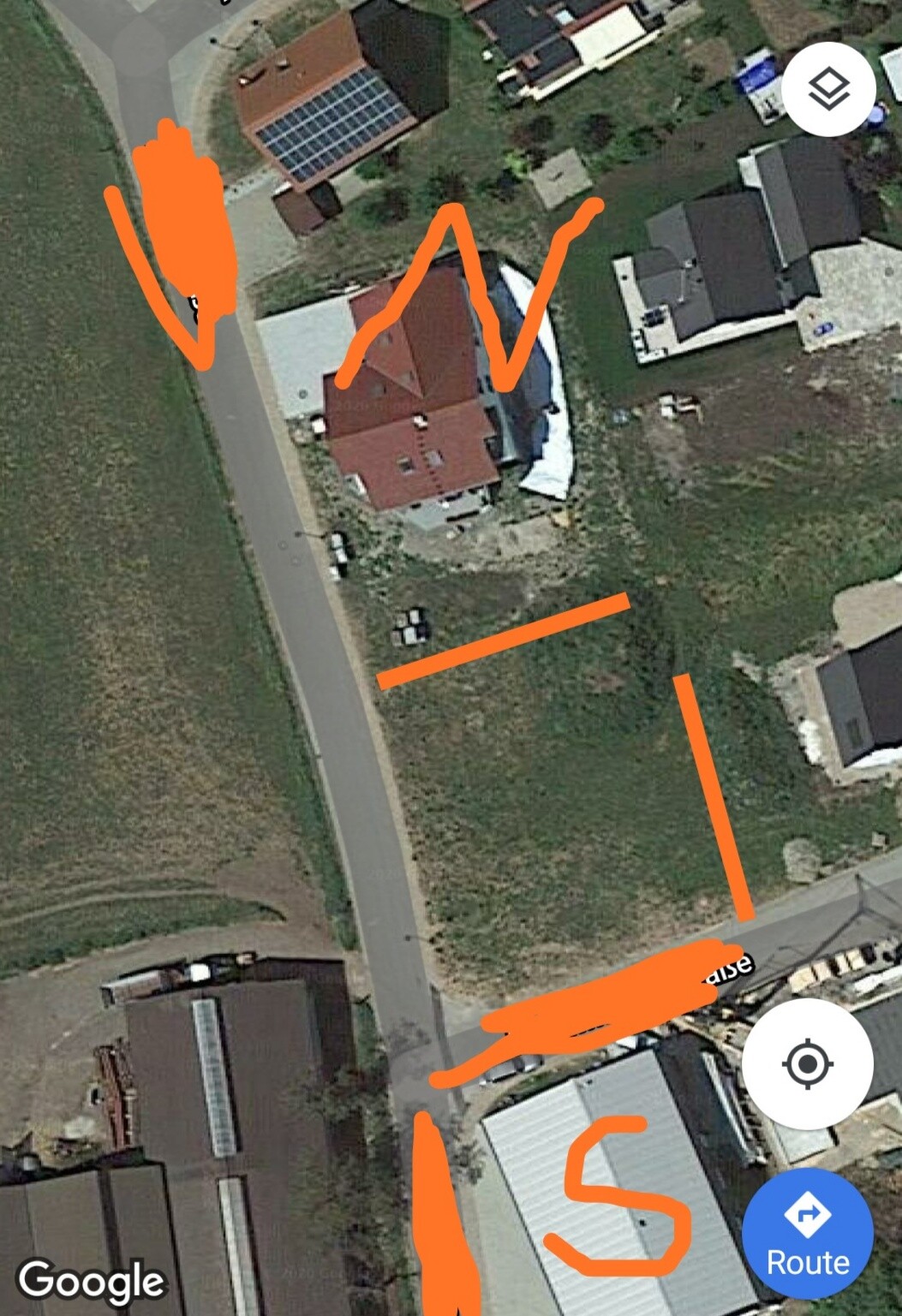 Satellitenaufnahme eines Wohngebiets mit roten Dächern, Straßen und orange Markierungen auf dem Gelände.