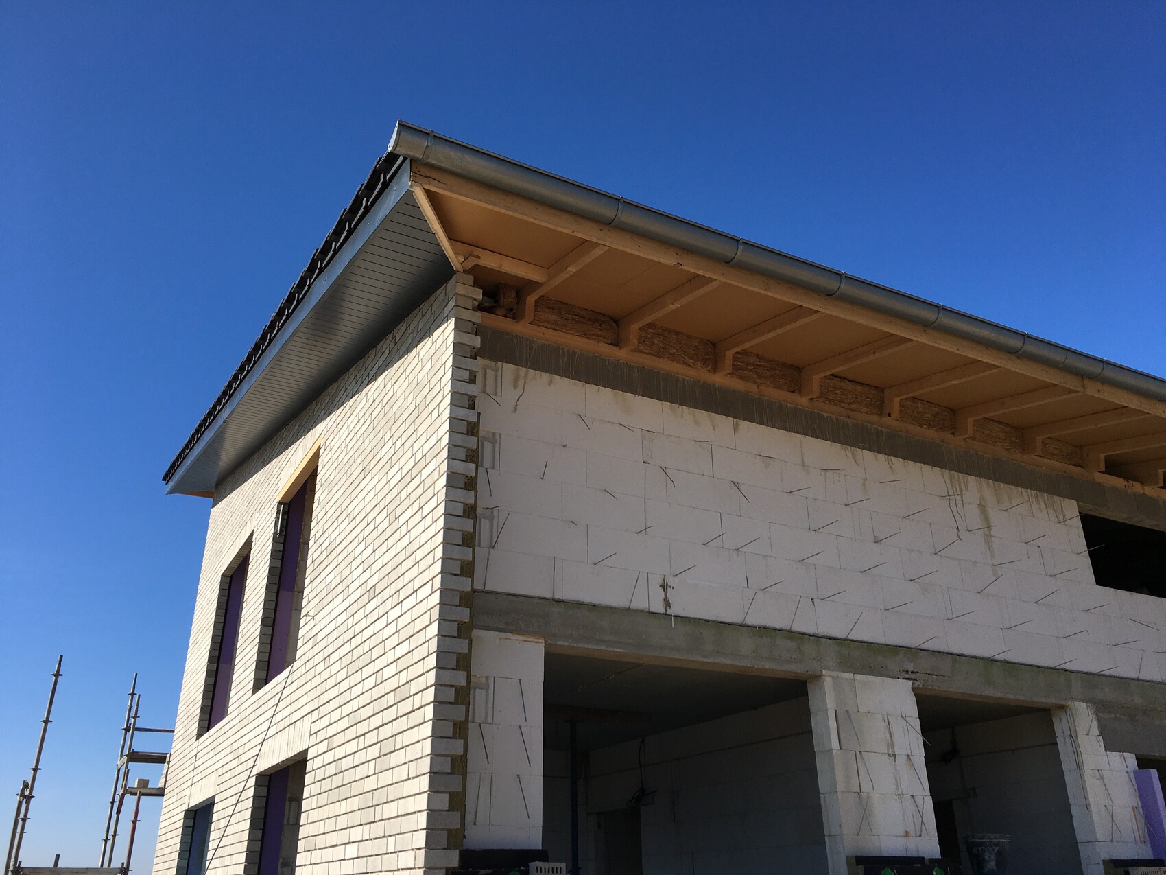 Zweistöckiges Haus aus weißen Blöcken im Bau, offenes Erdgeschoss, links Gerüst, blauer Himmel