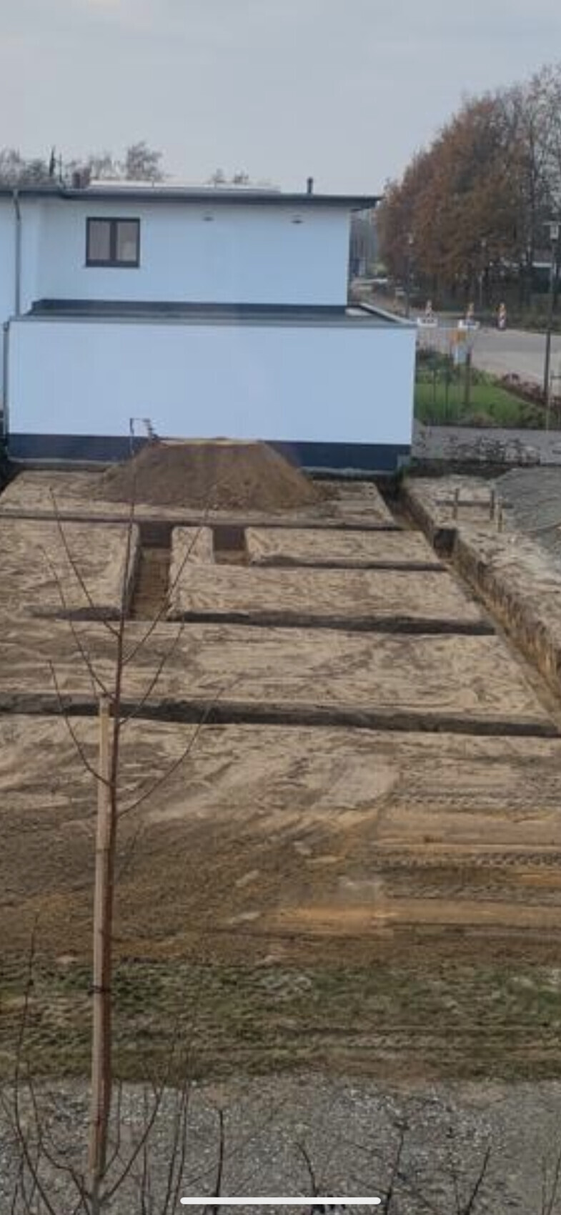 Weiße zweistöckige Bauweise hinter Baustelle mit Erdarbeiten und Gräben.