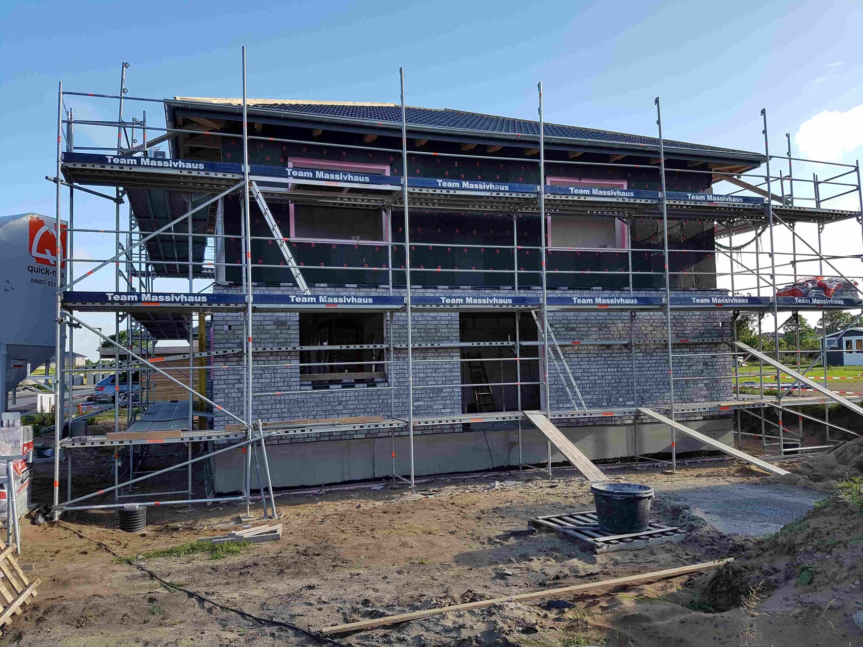 Rohbau eines Hauses mit Gerüst, Bauarbeiten und Baumaterialien auf der Baustelle.