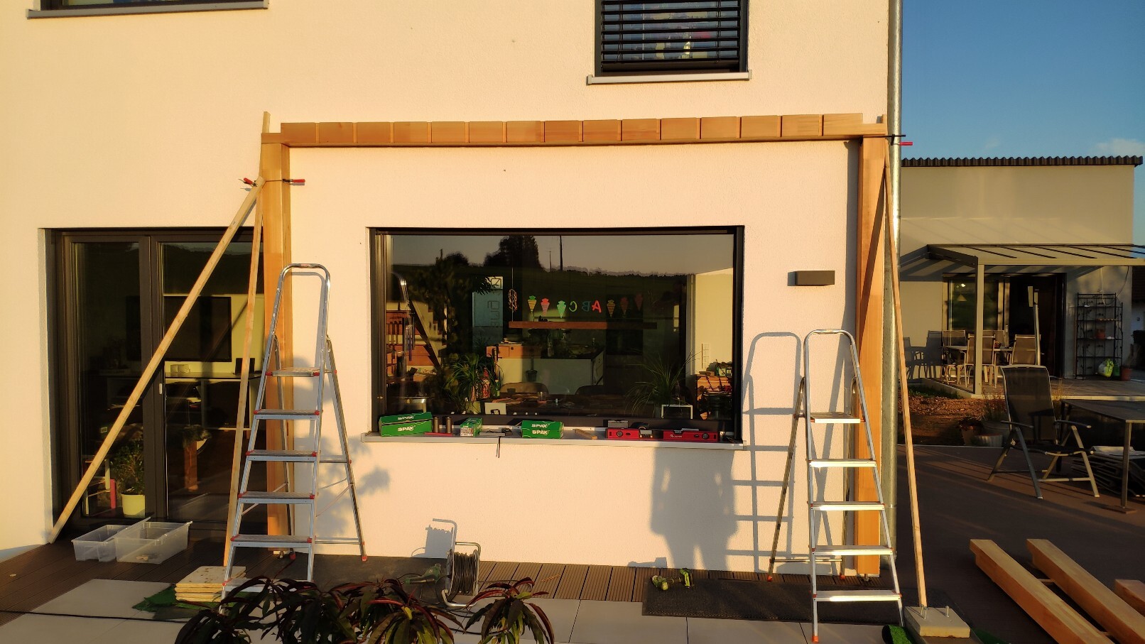 Außenansicht eines Hauses im Bau mit Holzrahmen über dem Fenster, Leitern und Werkzeugen davor.
