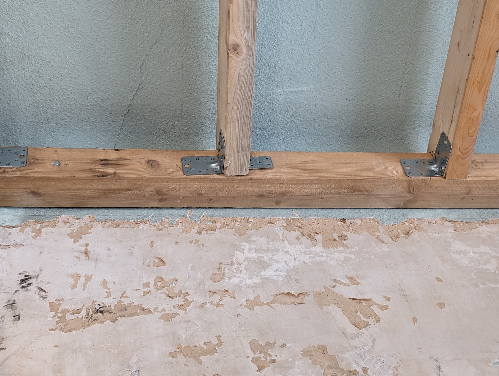 Holzbalken mit vertikalen Ständern und Metallwinkeln an einer blau gestrichenen Rohbau-Wand.