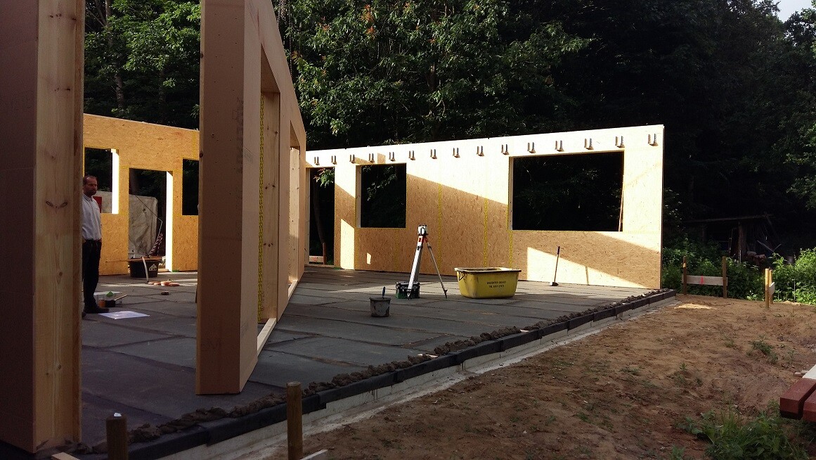 Baustelle mit Holzrahmenbau, unfertige Wände und Fensteröffnungen, Werkzeuge im Vordergrund.