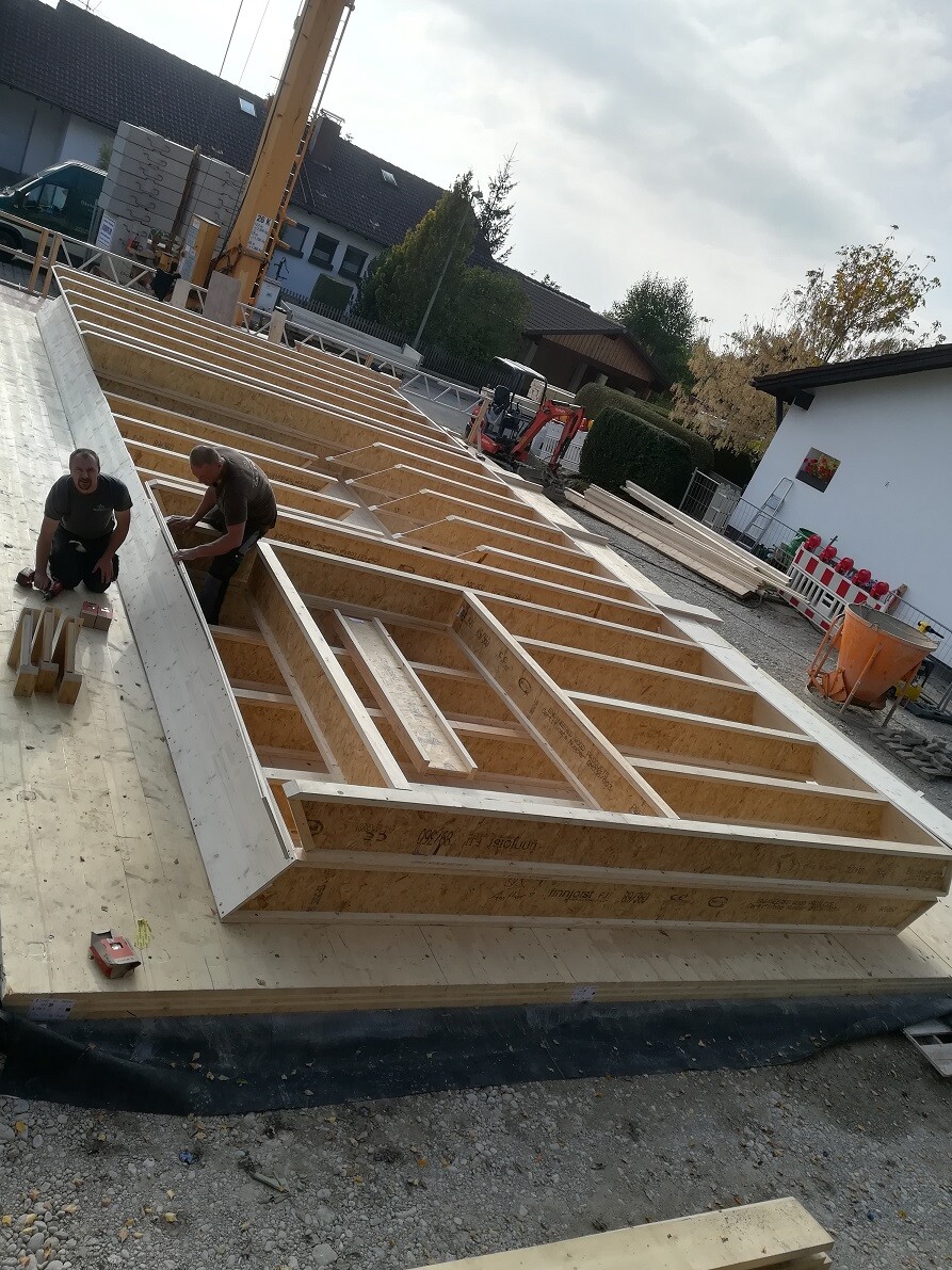 Baustelle mit Holzrahmen-Rohbau und zwei Bauarbeitern bei der Montage