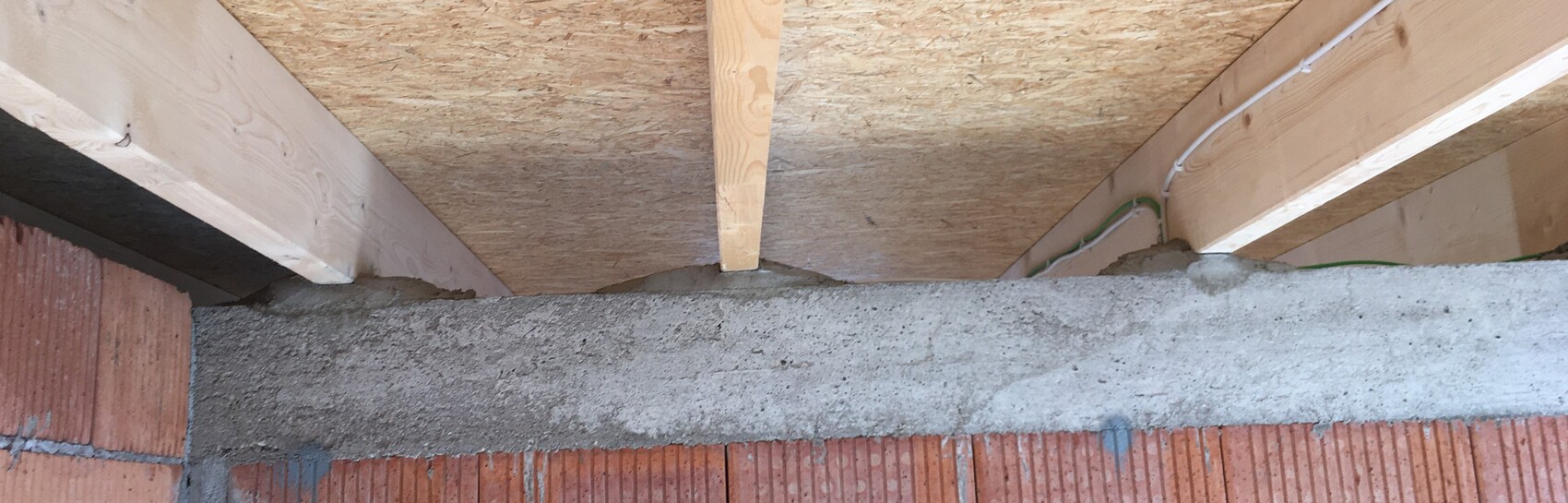 Ungefähre Innenansicht einer Baustelle: Holzbalken, OSB-Platte, Ziegelwand und Kabel.