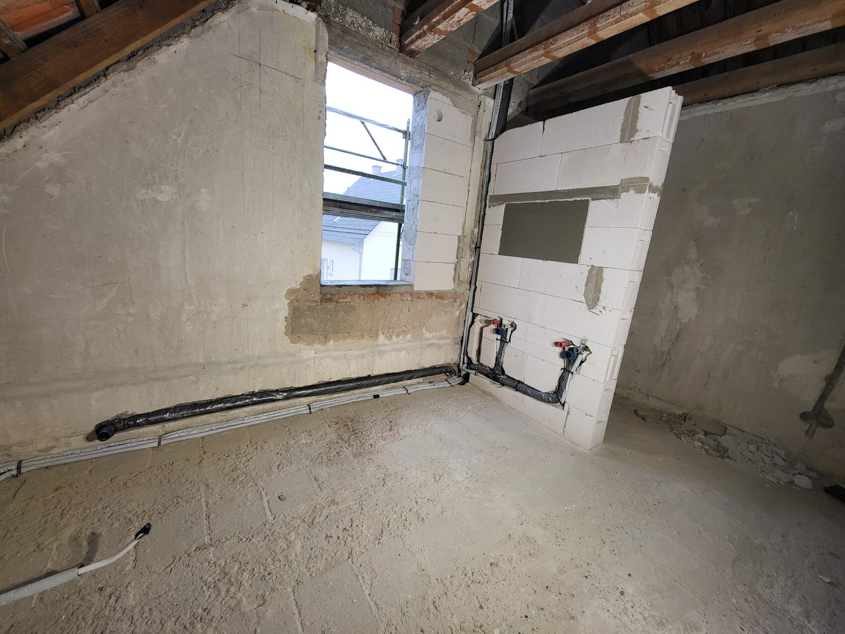 Rohbau-Innenraum mit Betonwänden, isolierten Rohrleitungen an der Wand und Fensteröffnung