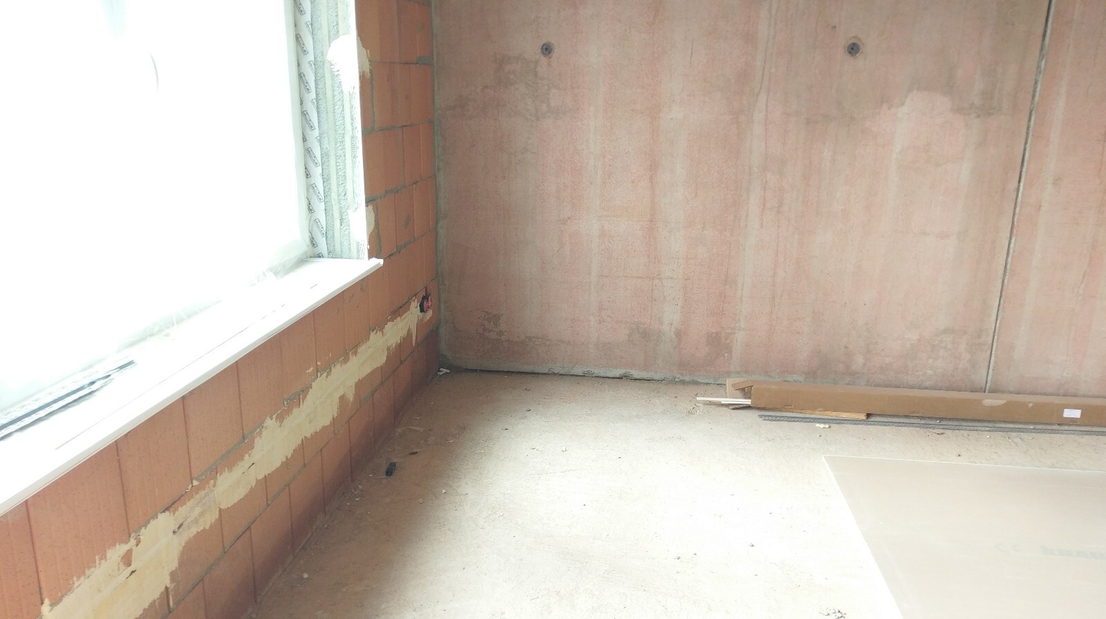 Unbearbeiteter Innenraum eines Neubaus mit rohen Ziegelwänden, Fensteröffnung und Baumaterial