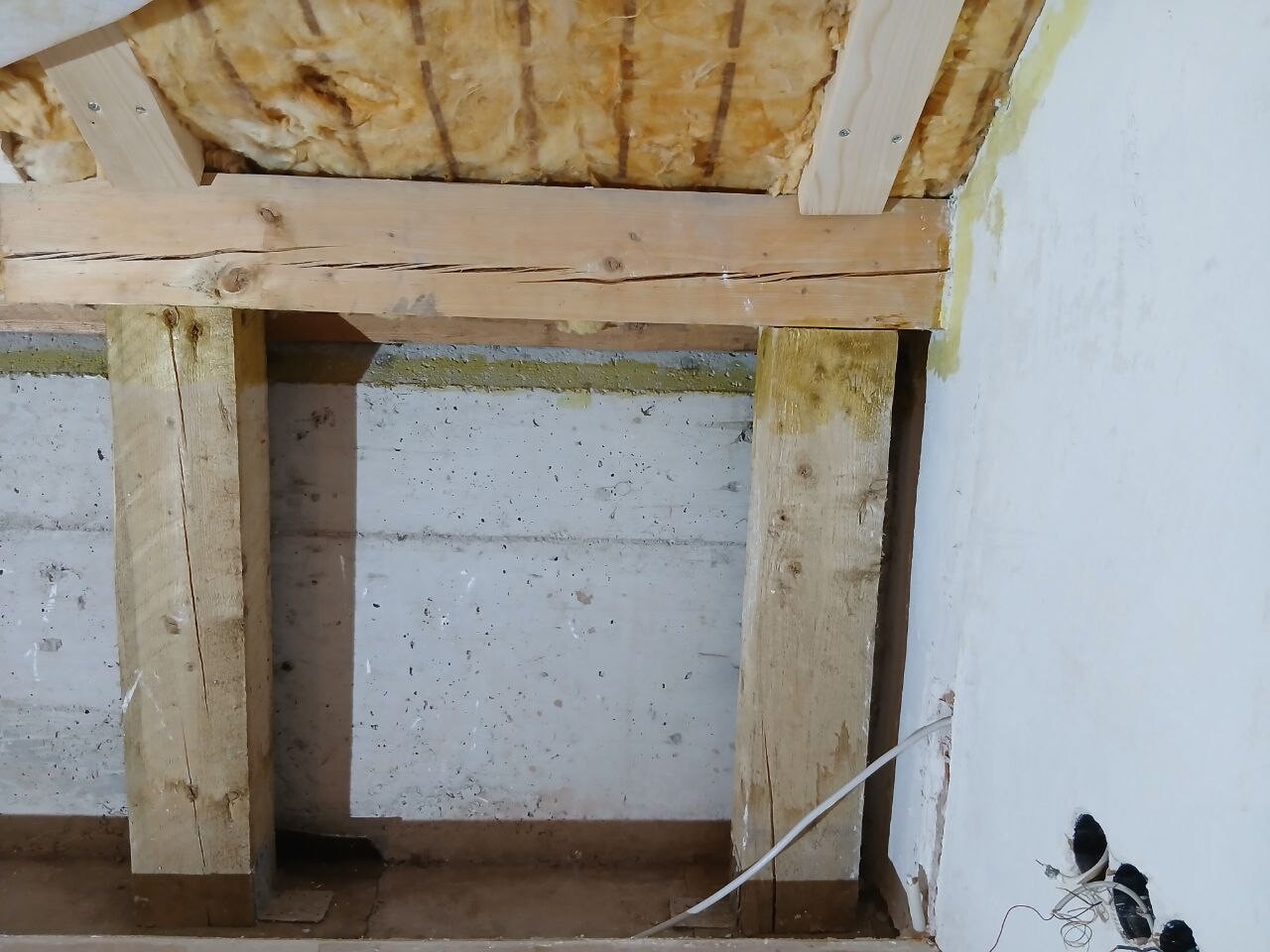 Rohbau Innenbereich mit Holzbalken, Dämmung und freiliegender Wandkonstruktion.