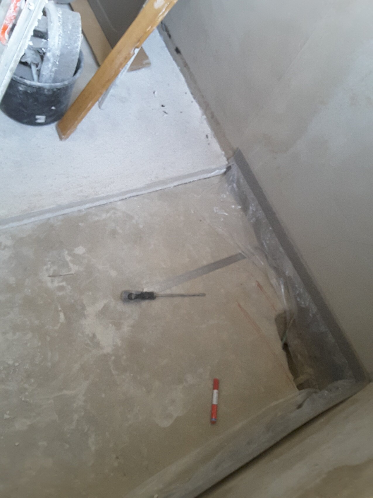 Unbearbeiteter Innenraum eines Bauprojekts mit Betonboden, Werkzeugen und Abdeckmaterial