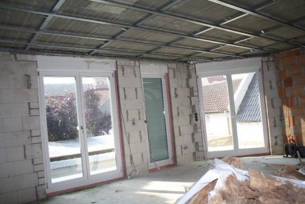Unfertiger Innenraum eines Hauses im Rohbau mit offenen Wänden, Fenstern und Baumaterial.