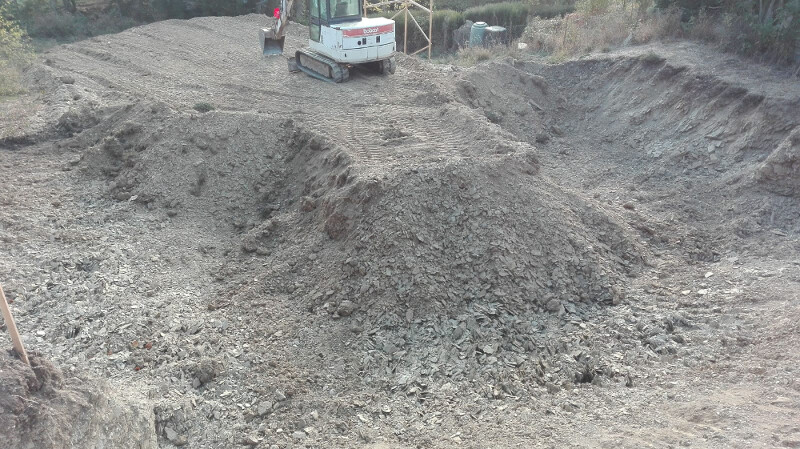 Kleiner Bagger auf Baustelle mit großen Erdmassen und Erdhügeln