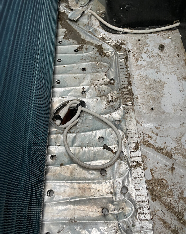Autoinnenboden eines Autos aus Metall mit Bohrungen, Schmutz und lose Kabelschlaufe.