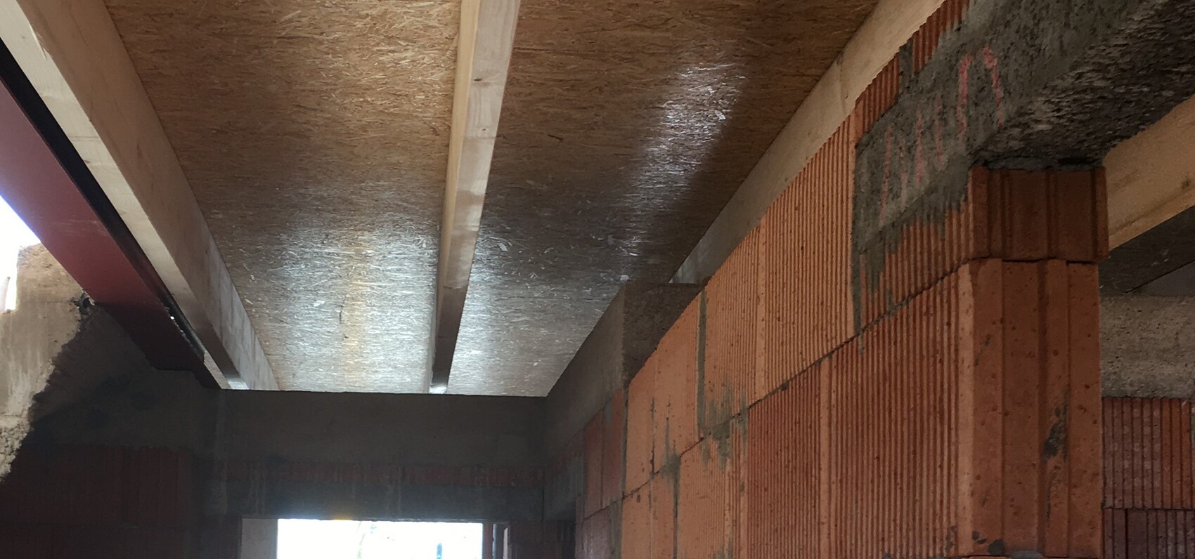 Baustelle: Innenraum mit rotem Ziegelmauerwerk, Stahlträgern und Holzbalkendecke.