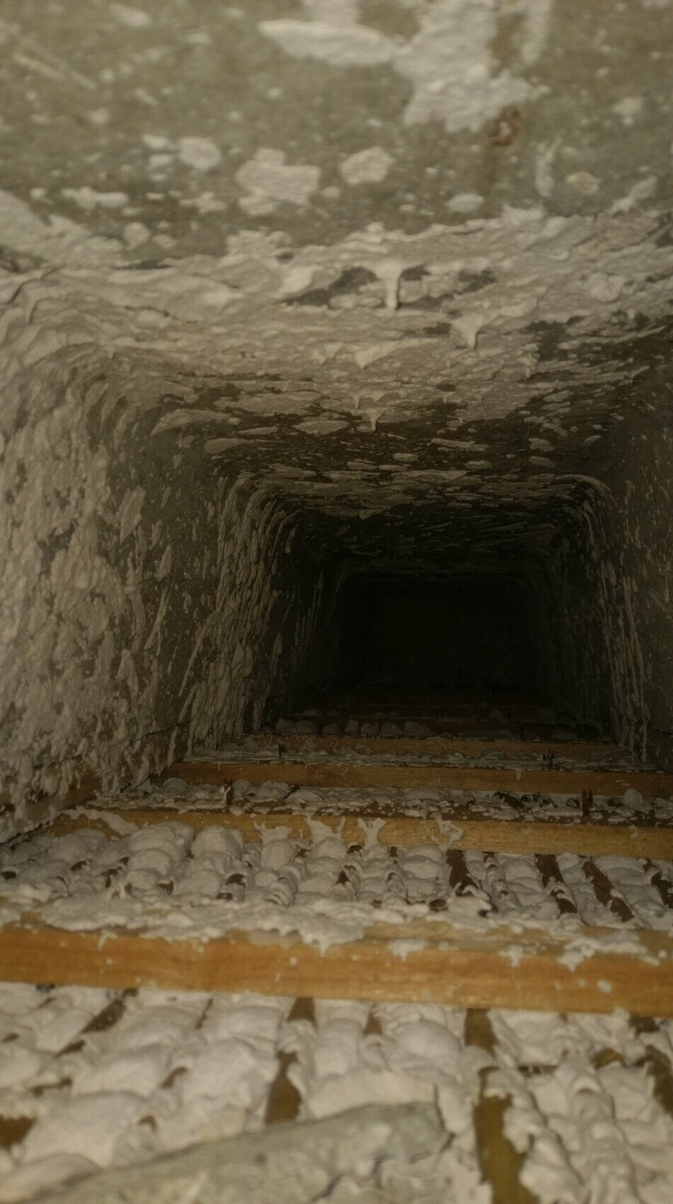 Schmaler, dunkler Schacht mit unregelmäßig verputzten Wänden und Holzbodenlatten.
