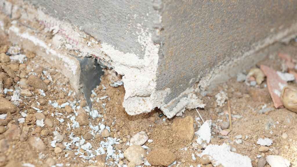 Beschädigtes Fundament an einer Betonwand mit Erdreich und Schutt.