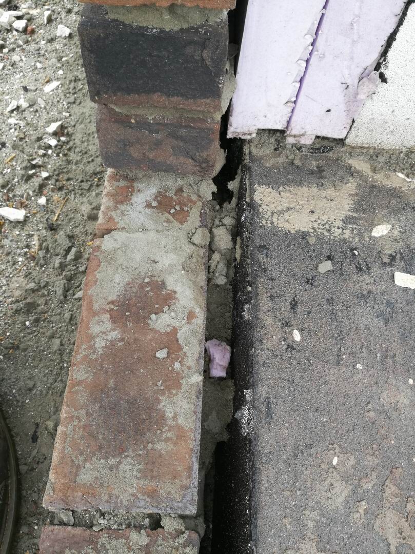 Offene Fuge zwischen Ziegelwand und Fundament mit bröckelndem Mörtel und Baustellenresten.
