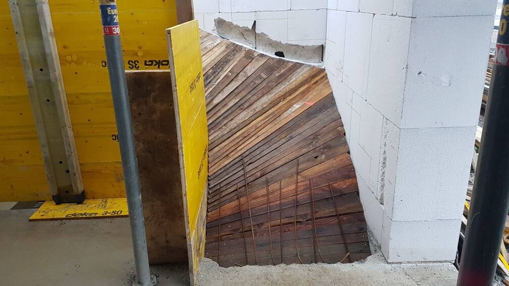 Baustelle: Rundholzform mit Bewehrung, gelbe Schalung, weiße Blockwand.